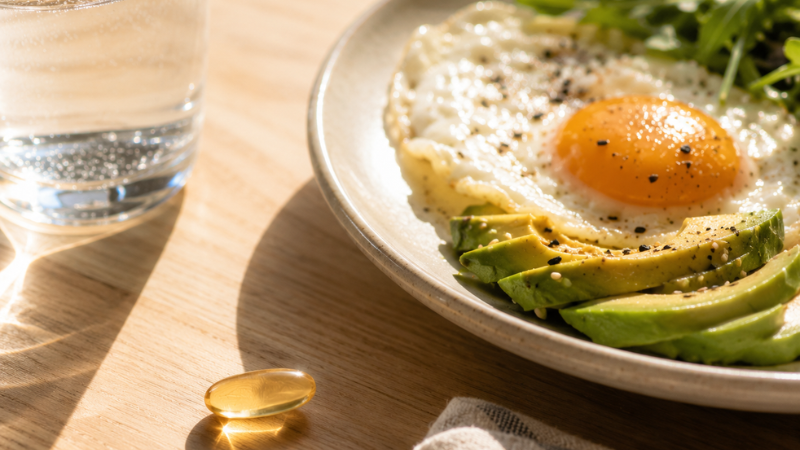Breakfast plate with eggs and avocado next to vitamin D supplement capsule showing the recommendation to take vitamin D with fat-containing food for better absorption