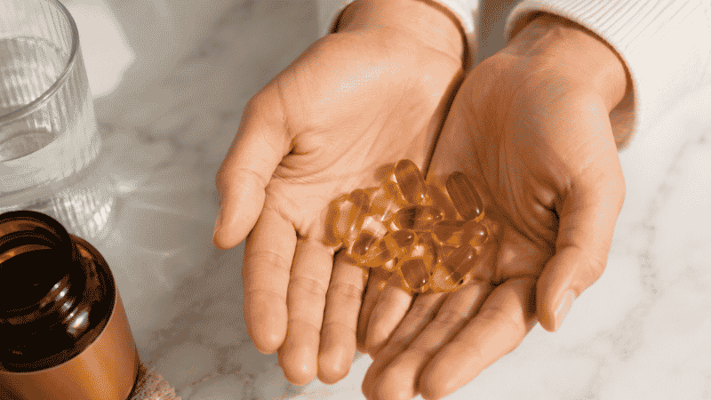 Person holding golden vitamin D3 softgel capsules representing the importance of understanding vitamin D side effects and safe dosage limits